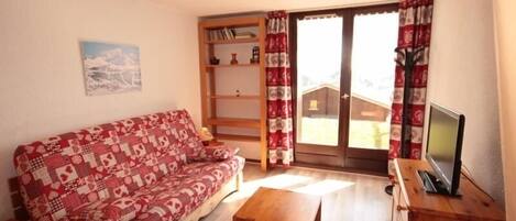 A cozy living room with a patterned sofa, a wooden coffee table, and a TV on a wooden cabinet.