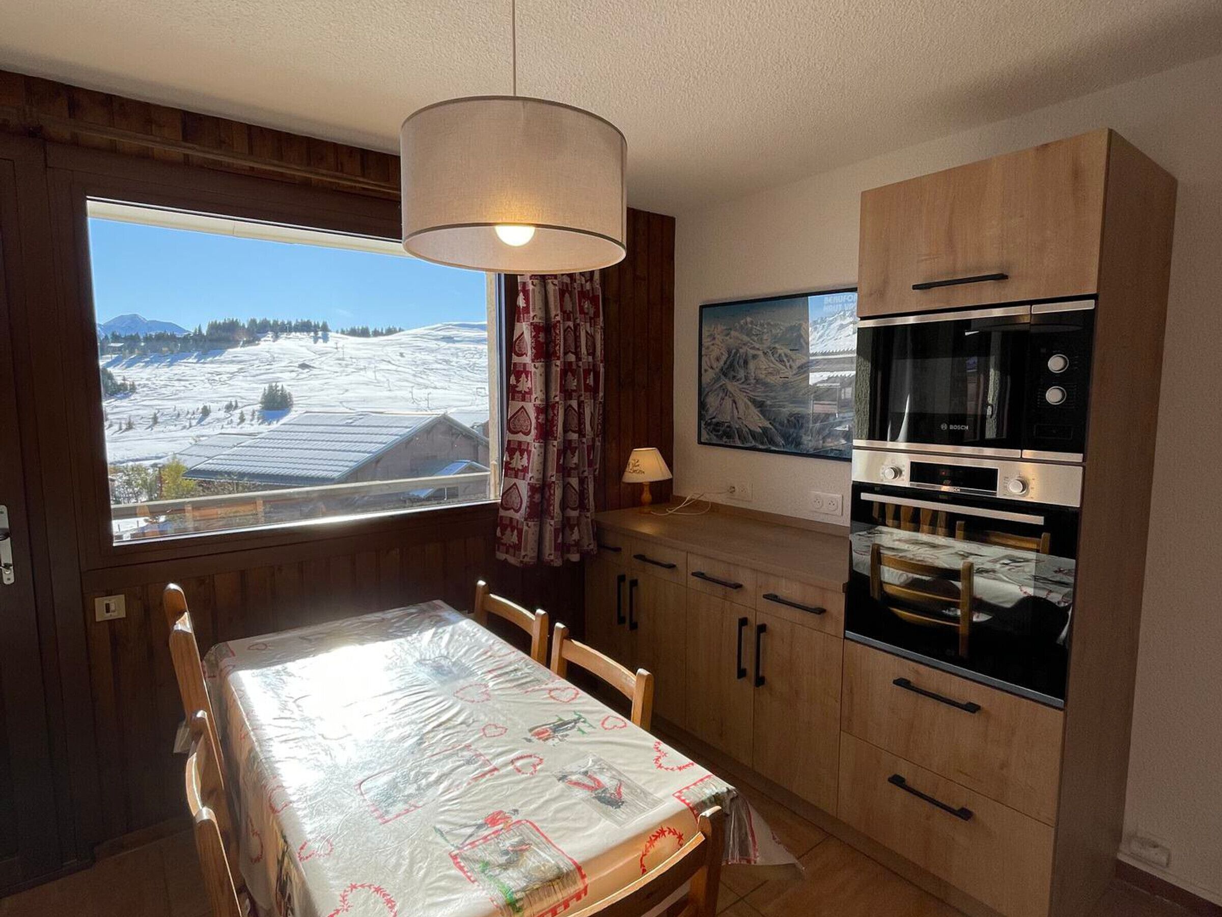 Eine Küche mit Holzausstattung, einem Bosch-Ofen und einem Esstisch mit Blick auf eine verschneite Landschaft.