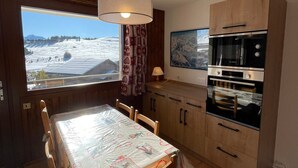 A kitchen with wooden cabinets, a Bosch oven, and a dining table with a view of a snowy landscape. - Bright cabin studio in Les Saisies, ski-in/ski-out, balcony, 5 sleeps (Hauteluce)