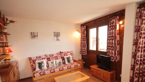 A cozy living room with a wooden sofa, a television, and a small wooden table. - Bright cabin studio in Les Saisies, ski-in/ski-out, balcony, 5 sleeps (Hauteluce)