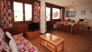 A cozy living room with a sofa, a wooden coffee table, a TV on a wooden cabinet, and a dining area with a table and chairs. - Bright cabin studio in Les Saisies, ski-in/ski-out, balcony, 5 sleeps (Hauteluce)