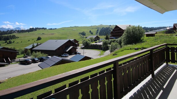 A balcony overlooking a rural village with traditional wooden houses, a clear sky, and a mountain range in the distance. - Bright cabin studio in Les Saisies, ski-in/ski-out, balcony, 5 sleeps (Hauteluce)