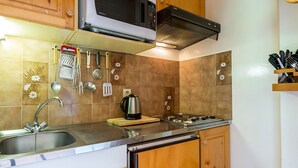 A kitchen with wooden cabinets, a stainless steel sink, a microwave, a kettle, and a stove.