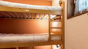 A bunk bed room with a wooden frame, a window with a net, and a small table.