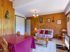 Una sala de estar acogedora con una pared de madera, un sofá con cojines coloridos, una mesa de centro y un comedor con mesa y sillas.
