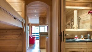A wooden interior with a sofa, a kitchen area, and a hallway leading to a window.