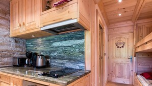 A wooden cabin interior with a kitchen area featuring a stone backsplash, a stove, and a coffee maker.