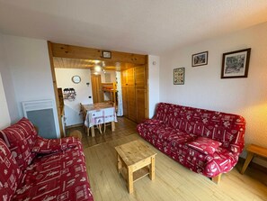 Una sala de estar con un sofá rojo estampado, una mesa de centro de madera y un comedor con una mesa dispuesta para dos.