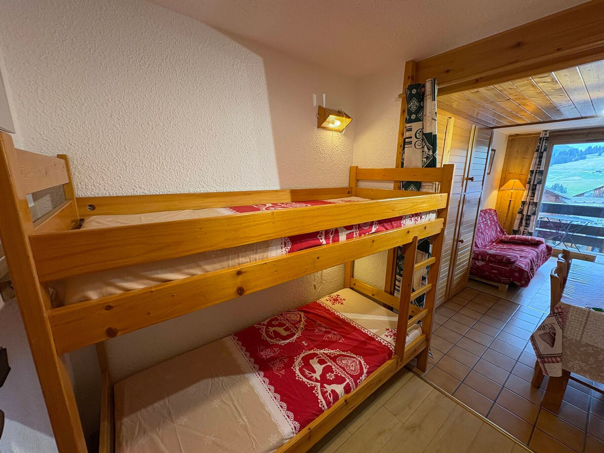 A bunk bed with a red and white patterned bedspread, a wooden headboard, and a wall-mounted light fixture.
