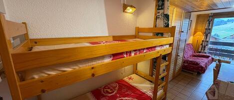 A bunk bed with a red and white patterned bedspread, a wooden headboard, and a wall-mounted light fixture.