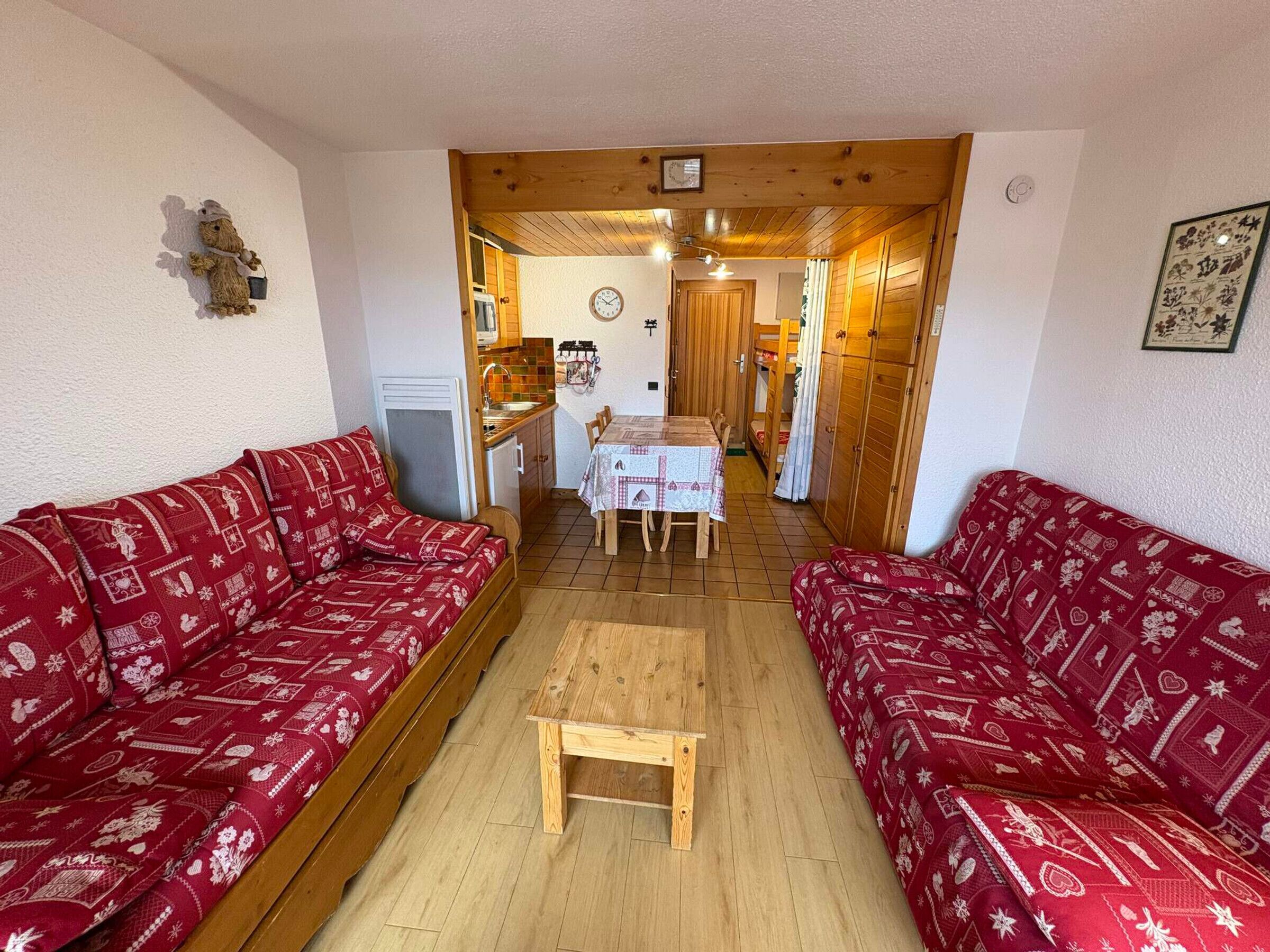 Ein kompakter Wohnraum mit zwei roten Sofas mit Muster, einem kleinen Holztisch, einer Küchenzeile und einem Essbereich.