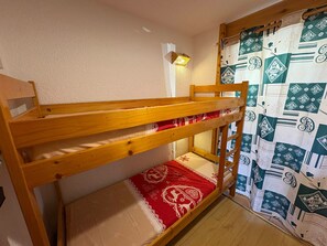 Una cama litera con colchón rojo y color beige, estructura de madera y una lámpara fijada a la pared.