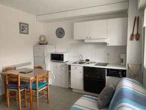 Una cucina funzionale con mobili bianchi, un forno a microonde, un lavello e una lavastoviglie. C'è un tavolo con sedie e un divano a righe.