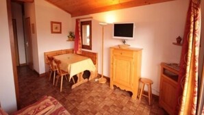 Una habitación acogedora con techo de madera, una mesa de comedor con sillas, un televisor sobre un mueble de madera y un taburete pequeño.