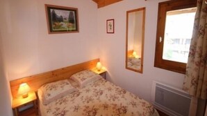Un dormitorio con techo de madera, una cama con ropa de cama floral, dos lámparas de noche, un cuadro enmarcado, un espejo y una ventana con cortinas.