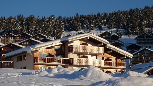 Un balneario de esquí cubierto de nieve con chalets de madera que tienen balcones y ventanas grandes.