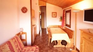 Una habitación acogedora con techo de madera, una mesa de comedor con sillas, un sofá y un televisor montado en la pared.