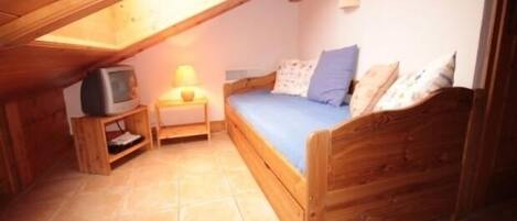 A small attic bedroom with a wooden bed, a nightstand, a television, and a lamp.