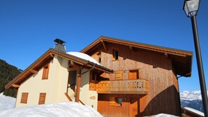 A wooden chalet with a balcony, surrounded by snow, with a clear sky and mountains in the background. - Stunning 4-Room Mezzanine with Parking and Pets Allowed (Villard-sur-Doron)