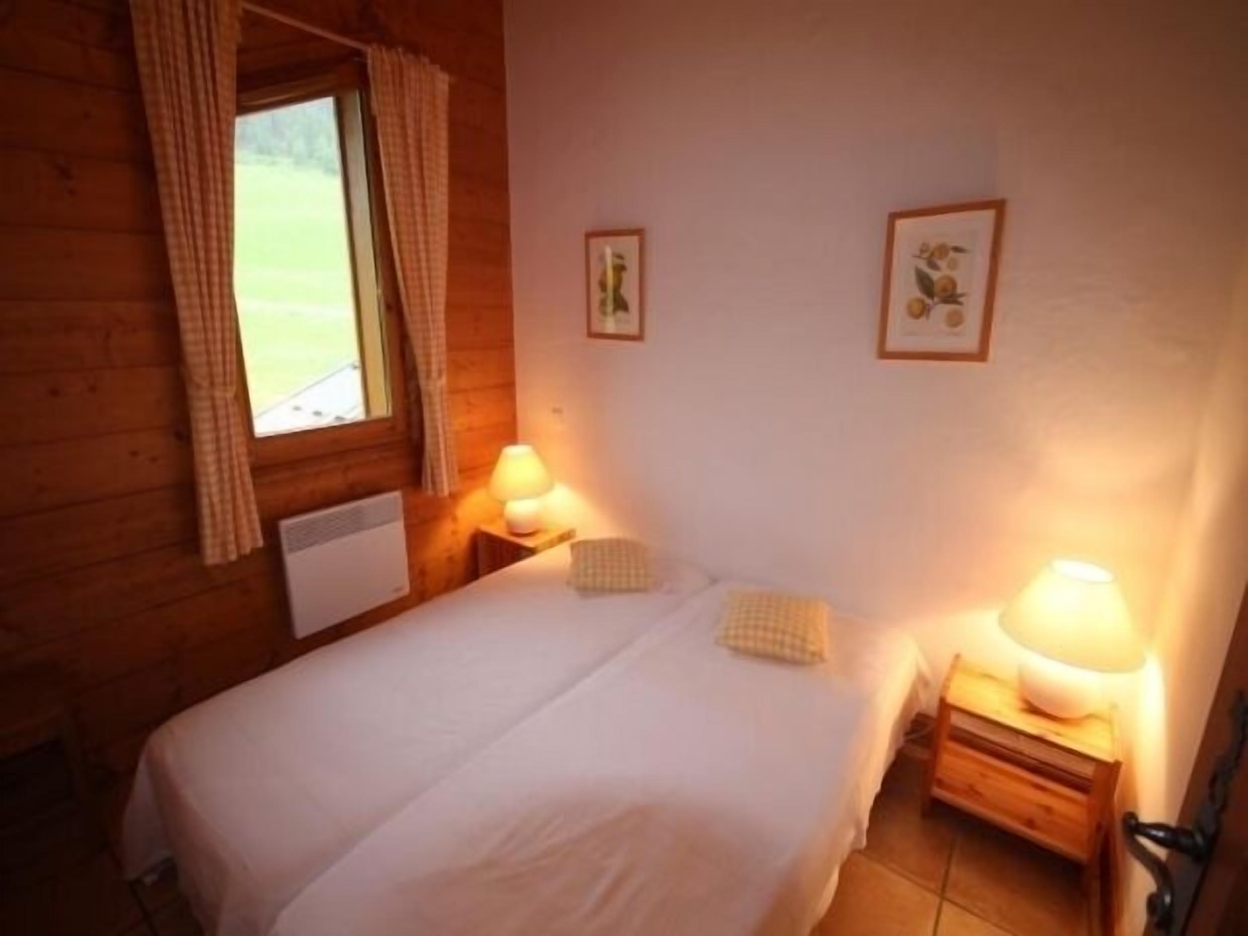 Een gezellige kamer met een bed, twee bedlampen en een raam met gordijnen.