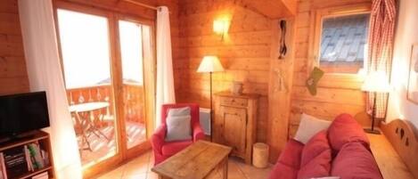 A cozy log cabin interior with a wooden ceiling, a sofa set, a television, and a dining table.