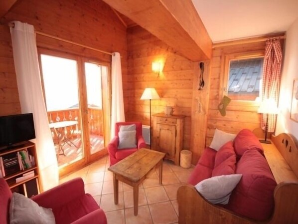 A cozy log cabin interior with a wooden ceiling, a sofa set, a television, and a dining table.