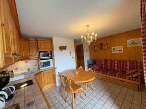 A cozy kitchen with wooden cabinets, a dining table with chairs, a chandelier, and a sofa with patterned cushions. - Cozy 3-room apartment, 6 pers, pets allowed (Les Saisies)