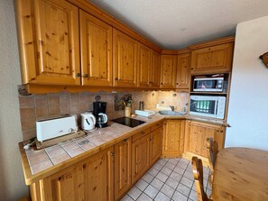 A kitchen with wooden cabinets, a tiled backsplash, a coffee maker, a toaster, and a microwave. - Cozy 3-room apartment, 6 pers, pets allowed (Les Saisies)