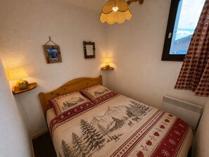A bedroom with a wooden bed, two wall-mounted lamps, a framed picture, and a window with curtains. - Cozy 3-room apartment, 6 pers, pets allowed (Les Saisies)