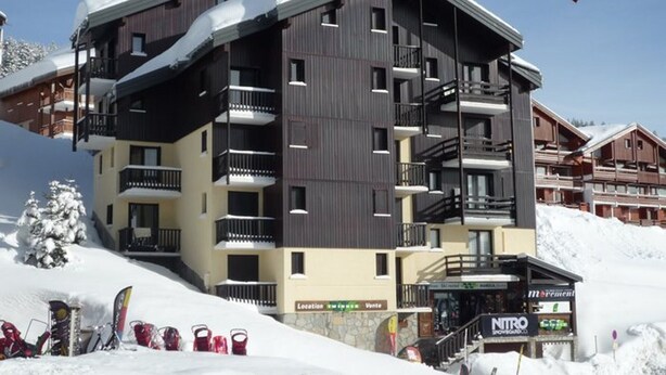Un hôtel à plusieurs étages, doté de balcons, d’un local pour le matériel de ski et d’une enseigne indiquant « NITRO ».