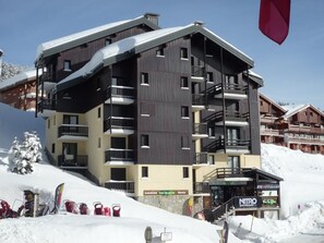 A multi-story hotel with balconies, ski equipment, and a sign for 'NITRO'. - Cozy 3-room apartment, 6 pers, pets allowed (Les Saisies)