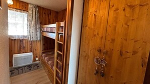 A bunk bed room with wooden walls, a radiator, and a window with curtains.