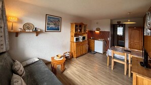 A cozy living room with a sofa, a small wooden table, and a kitchen area with wooden cabinets and a refrigerator.