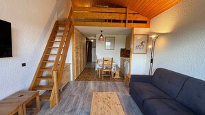 Una sala de estar acogedora con una escalera de madera, un sofá, una mesa de centro y un comedor con mesa y sillas.