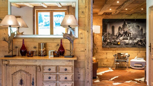 A rustic interior with wooden walls and a large mirror above a wooden cabinet with drawers.