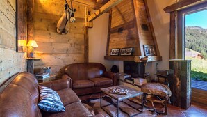 A rustic cabin interior with leather sofas, a fireplace, wooden walls, and a view of the outdoors.
