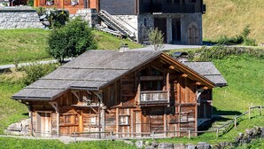 A rustic wooden cabin with a steeply pitched roof, a balcony, and a stone foundation.