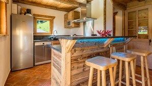 A kitchen with wooden beams, a stainless steel refrigerator, a dishwasher, and a wooden bar with stools.