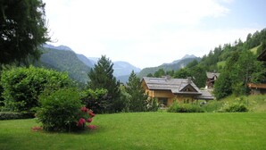 Ein Haus mit geneigtem Dach, umgeben von einem gepflegten Rasen und verschiedenen Bäumen und Sträuchern.