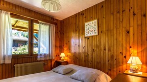 Ein Zimmer mit Holzwänden, einem Bett, zwei Nachttischlampen, einem Fenster mit Vorhängen und einem gerahmten Bild an der Wand.