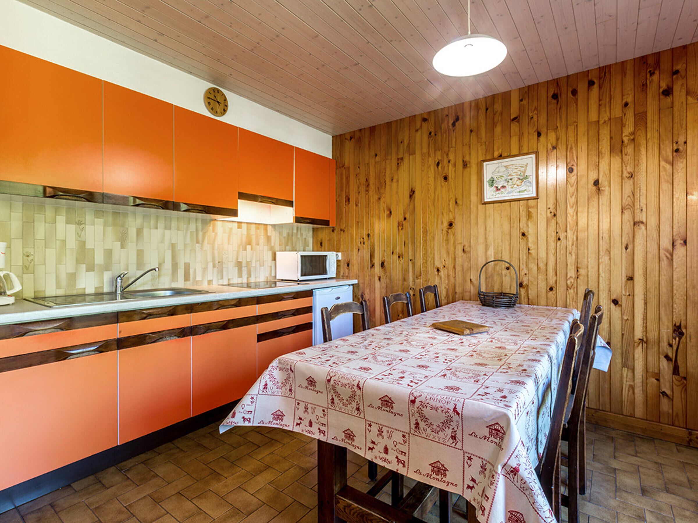 A kitchen with orange cabinets, a microwave, and a dining table with a tablecloth.