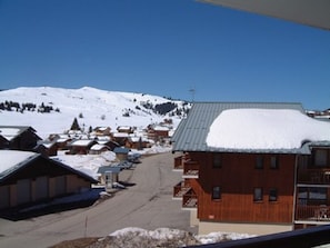 A snow-covered building with a metal roof, surrounded by other buildings and a snowy mountain in the background.