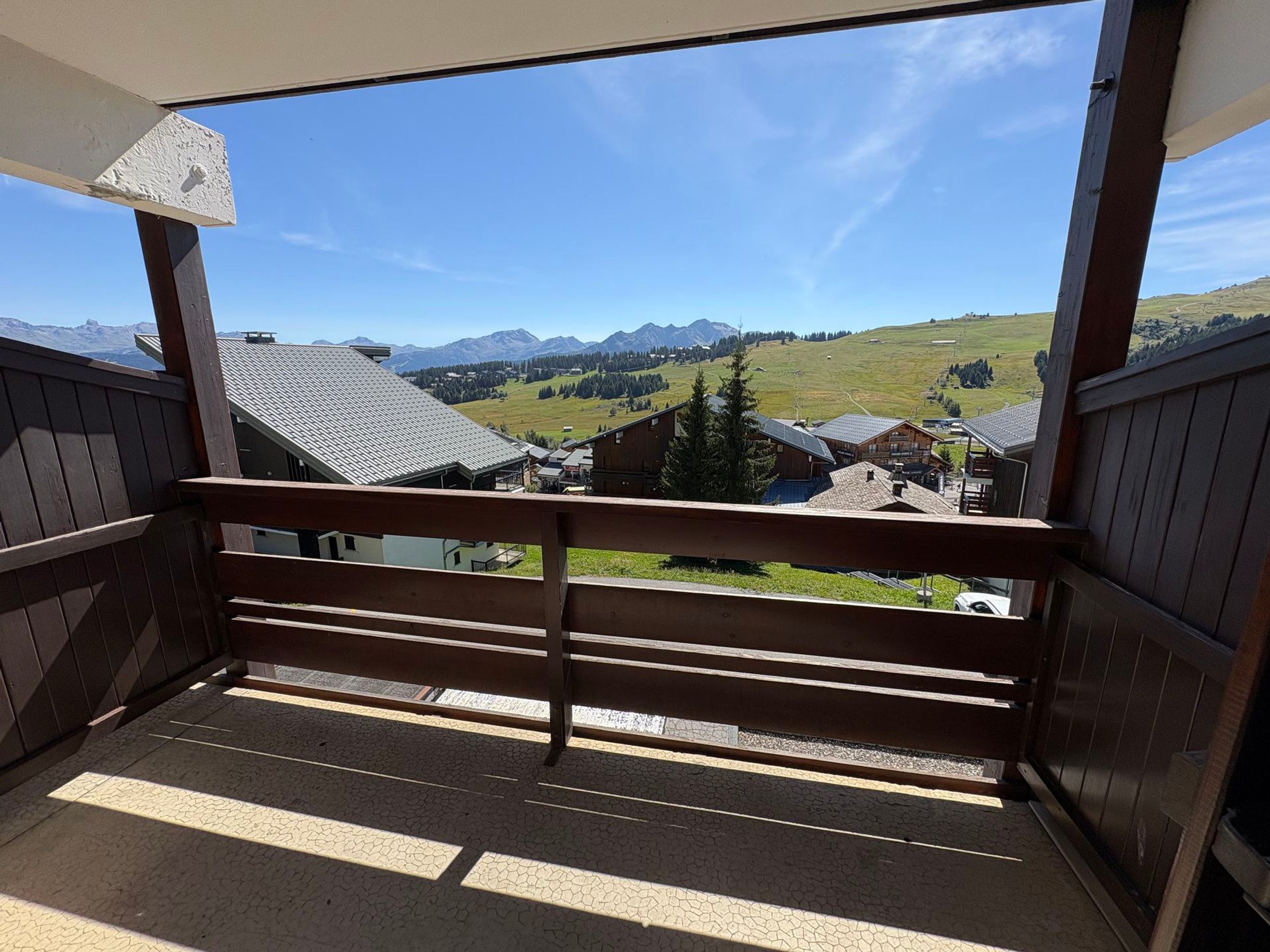 A balcony with a view of a mountain landscape, wooden railings, and a tiled floor.