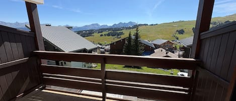 A balcony with a view of a mountain landscape, wooden railings, and a tiled floor.