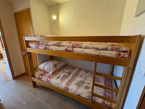 Una cama litera con ropa de cama estampada en una habitación con suelo de madera y una puerta.