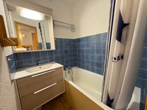 A bathroom with a white sink, wooden cabinet, and a bathtub with a shower curtain. - Les Saisies - Studio Cabin 4 People, South (Les Saisies)