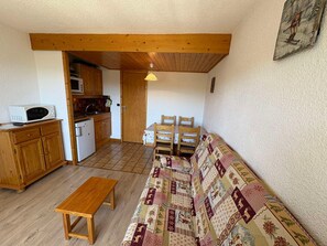 Un espacio habitable funcional con kitchenette, un banco de madera, un sofá estampado y un comedor con sillas.