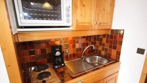 Una cocina compacta equipada con microondas, cafetera, lavabo y estufa.