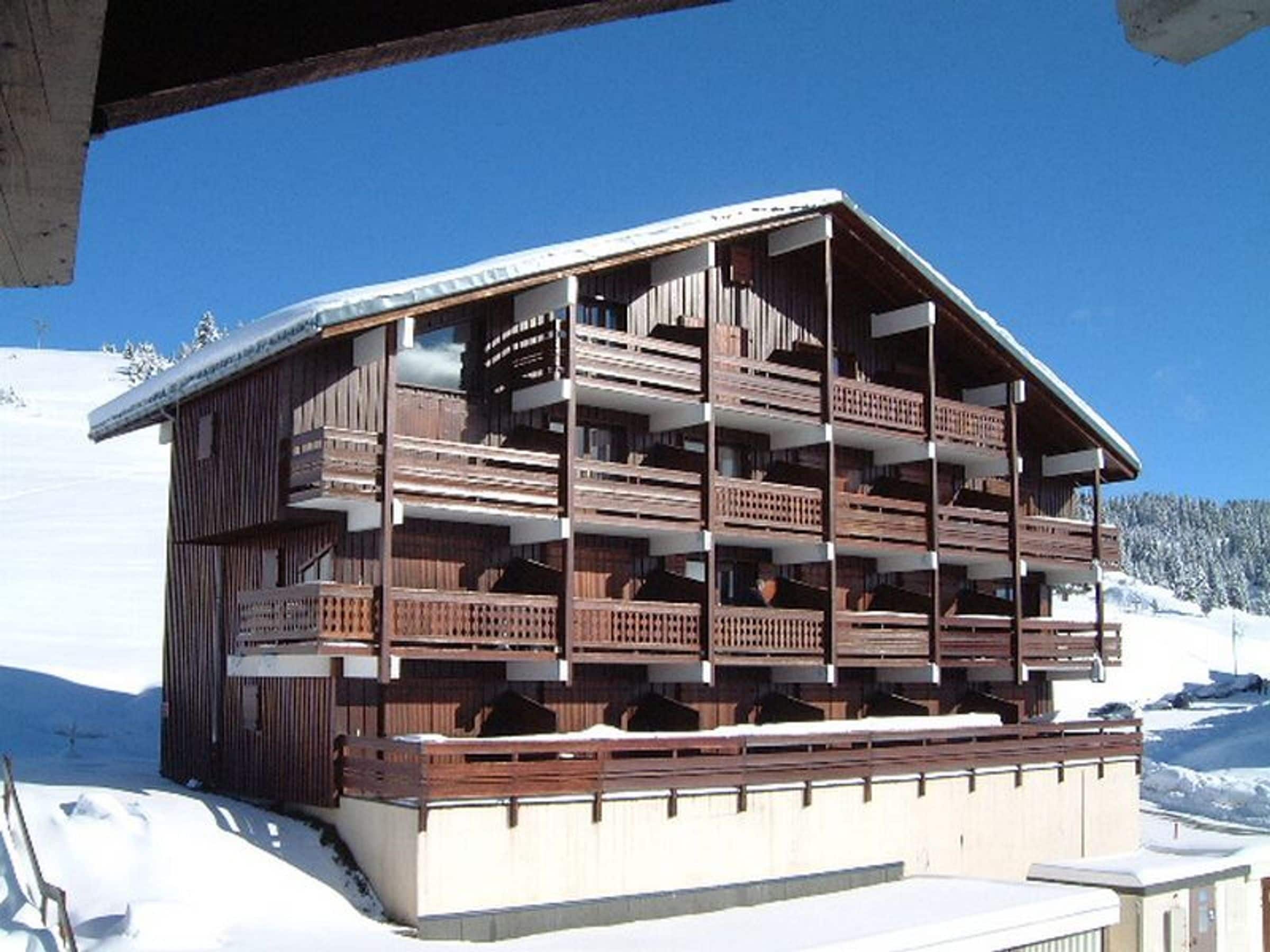 A multi-story wooden chalet with balconies, situated on a snowy mountain.