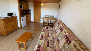 A compact living space with a wooden bench, a patterned sofa, a dining table with chairs, a kitchen area with a microwave and refrigerator, and a wooden ceiling. - Les Saisies - Studio Cabin 4 People, South (Les Saisies)